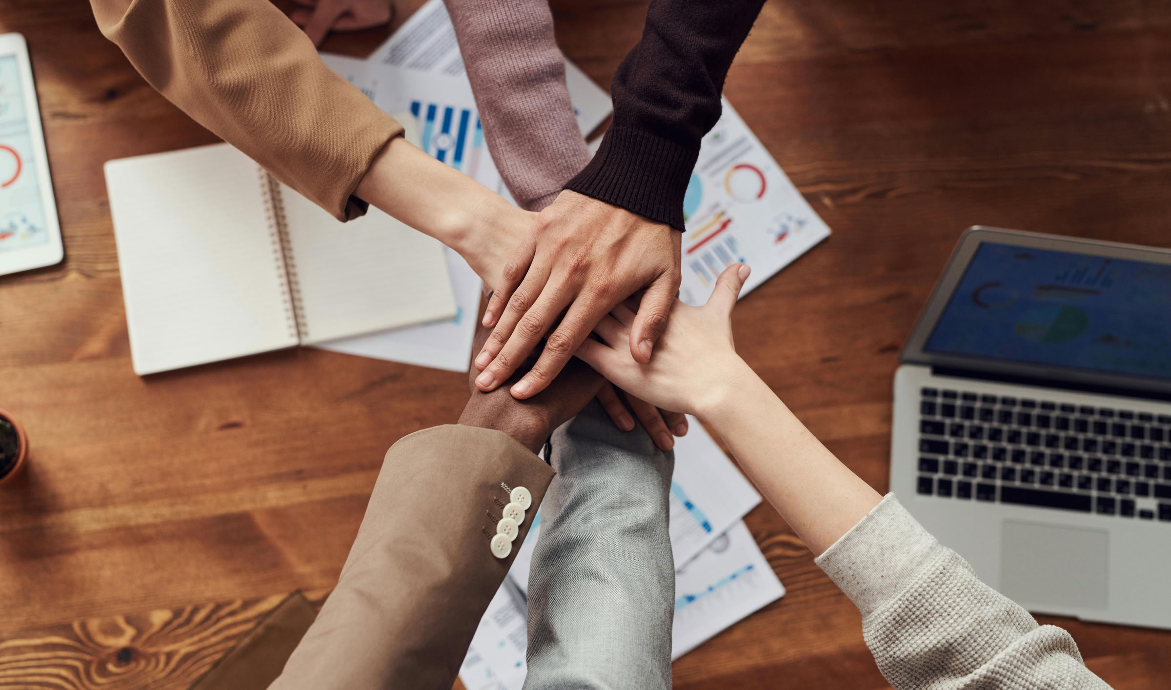 Diverse professionals unite for teamwork around a wooden table with laptops and documents.